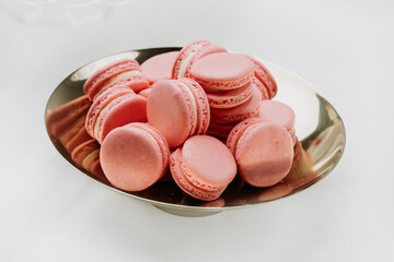A stylish arrangement of pink macarons on a reflective silver plate, creating a modern and elegant...