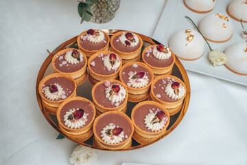 A tray of exquisite chocolate tarts garnished with whipped cream and dried rosebuds. The delicate dessert presentation on a gold tray adds a touch of sophistication and luxury to any dessert table.