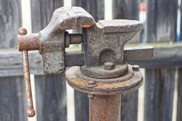 some iron old retro mechanical adjustable rusty dirty with handle closed industrial heavy duty vice bolted to pole near wooden fence day outside