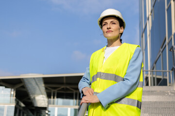 Portrait of a confident female engineer in a safety vest, with a modern building in the background. Copy space.