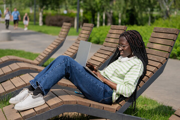 Young freelancer is working on her laptop while enjoying a beautiful day in the park, finding a...