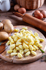 Uncooked homemade potato gnocchi on cutting board over wooden table with flour. See series.
