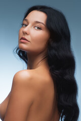 Fototapeta premium Portrait of an elegant bare beauty woman with long black hair, posing with a serene expression against a blue gradient background.