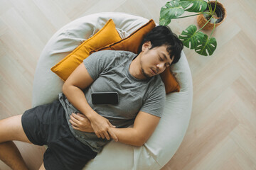 Asian man sleep over the phone on the bean bag sofa, taking a nap in the afternoon.
