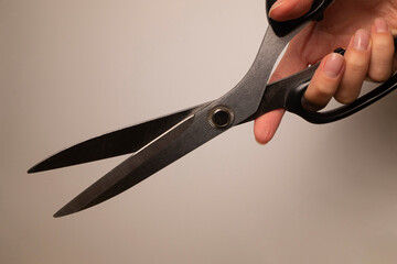 Female hand holding fabric scissors with smooth steel blade and black plastic handles on a white background.