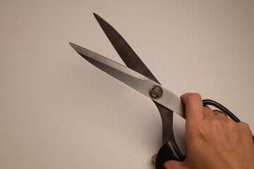 A woman's hand holds a fabric scissors with steel blades in a black handle on a white background.