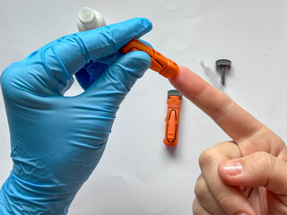 medical professional using a lancet to collect a blood sample from the fingertip of a female patient