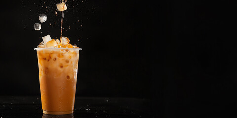 Ice cube falling into a plastic takeaway cup of Thai iced tea on a black background with copy space
