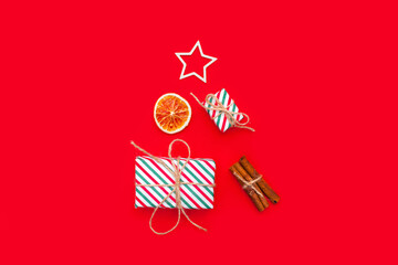 Collection of Christmas objects - goft box, eve fir, dried orange, pine cone, star cinnamon on red background. New Year and winter minimal holiday frame composition. Flat lay, top view, place for text
