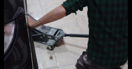 Mechanic lifting a car with a hydraulic jack in a workshop