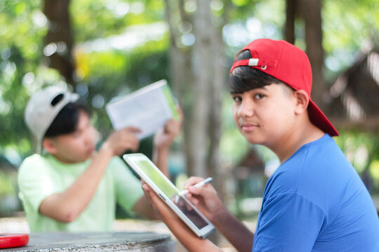 Asian schoolboys are studying high level of trees in school botanical garden by using inclinometer and measure tape and looking up for measuring high level of trees and saving information into taplet.