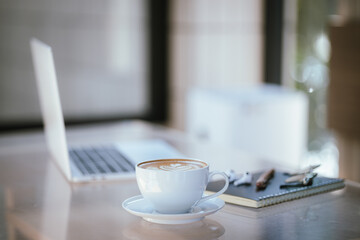 A cup of coffee is placed near a laptop on a table with space for copying documents, suggesting a break from work or a relaxing time at a cafe.