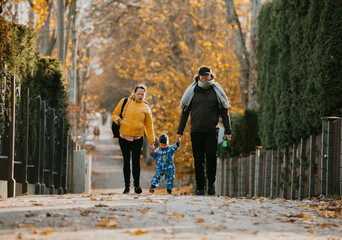 A loving couple strolls through a sunlit park with their young son, surrounded by the vibrant colors of autumn, enjoying a joyful and peaceful family moment together.