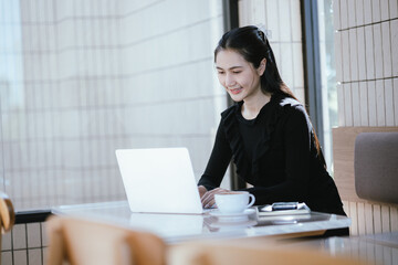 People relaxing in cafe concept. Happy face of adult Asian woman using smartphone on table with laptop computer and drink.