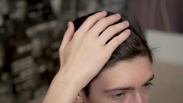 Teenager runs hand through black hair on head. Adolescent boy touches dark hair with hand. Young male slides fingers through jet black hair