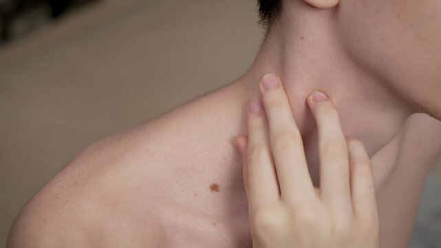 Shirtless teenager touches sore neck after strain. Adolescent boy without shirt holds painful neck from recent strain. Young male with no shirt rubs neck feeling discomfort of muscle strain