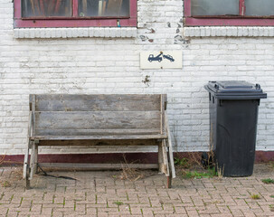 wooden bench and a black waste bin stands outside in front of a white painted stone wall