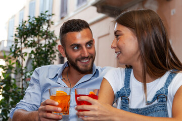 beautiful couple of smiling young adult lovers drinking cocktails sitting at a table in an outdoor pub