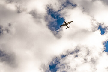 Fototapeta na wymiar A small airplane is captured flying above, framed by large, billowy clouds with a patch of blue sky peeking through. Dramatic perspective against the cloudy sky evokes a sense of adventure and flight.