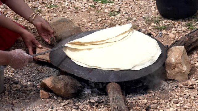 Woman is baking traditional iranian flat bread on a saj, a convex metal griddle, over an open fire