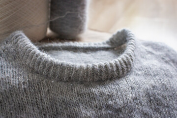 Gray cardigan sweater on wooden background, close up. Warm winter clothing. Rib sweater neck. Grey knitted sweater. Knitting pattern background. Cozy handmade clothes. Craft product close up