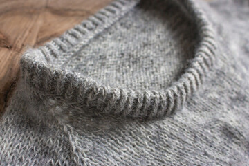 Gray cardigan sweater on wooden background, close up. Warm winter clothing. Rib sweater neck. Grey knitted sweater. Knitting pattern background. Cozy handmade clothes. Craft product close up