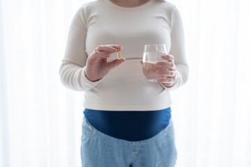 Pregnant woman holding a glass of water, taking vitamins during pregnancy. Pregnancy, health, pharmaceuticals. Close up