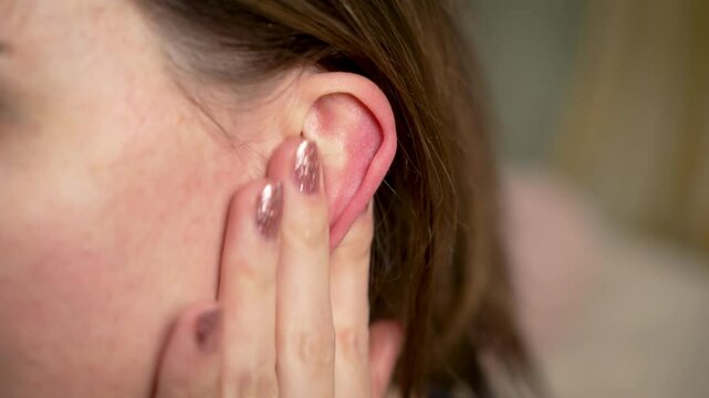Woman touching inflamed ear due to infection, otitis or earache. Female gently holding swollen ear caused by otitis media infection or inflammation. Painful otitis externa ear infection or
