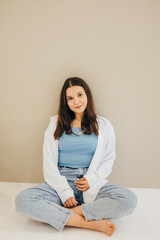 A woman in a white shirt and jeans stands by a wall, showing a stylish and understated look. The light background and natural pose give the shot a modern feel.