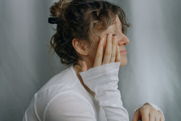 Sad woman with curly hair and white shirt is touching her face with her hand, suffering from depression and feeling lonely