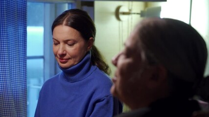 Adult 44 year old woman having lively conversation with elderly woman sitting at table in living room. Women laugh while talking.