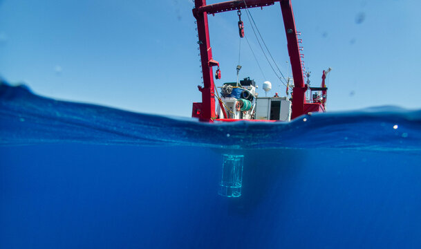 A research vessel floats over the deep blue ocean with submerged equipment prepared for scientific exploration.