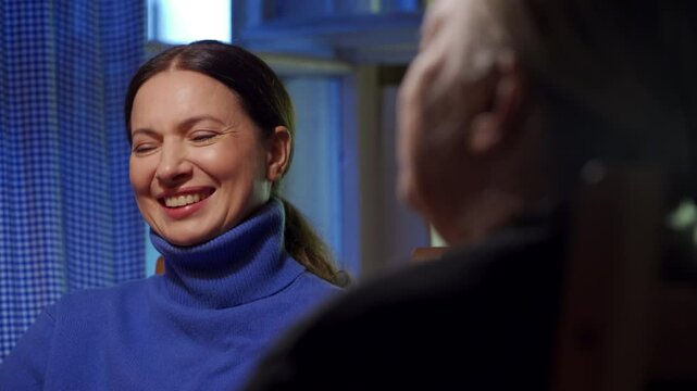 Adult 44 year old woman having lively conversation with elderly woman sitting at table in living room. Woman with a tense face listens, talks and laughs.