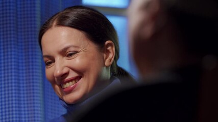 Adult 44 year old woman having lively conversation with elderly woman sitting at table in living room. Woman with a tense face listens and smiles.