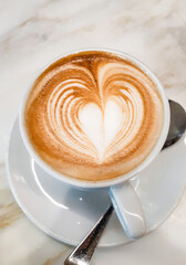 Creamy cappuccino with heart shaped latte art on marble table