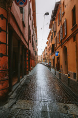 Rain slicked cobblestone street reflecting the warm orange hues of traditional italian buildings in bologna, italy, creating a picturesque urban scene