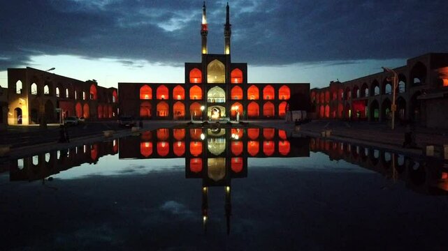 Amir chakhmaq mosque glows red at night, creating a stunning reflection in a still pool of water