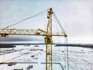 A tall yellow construction crane stands high against a snowy landscape during winter, overlooking a...