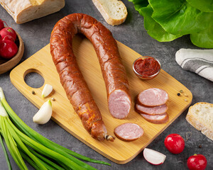 Delicious traditional sausage displayed on a wooden cutting board with fresh vegetables and bread...