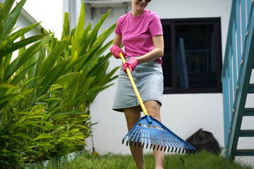 A woman raking the lawn at the backyard of her house 