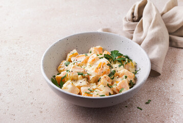 Bowl of pumpkin in sour cream sauce sprinkled with fresh parsley on beige textured stone table. Vegetarian food