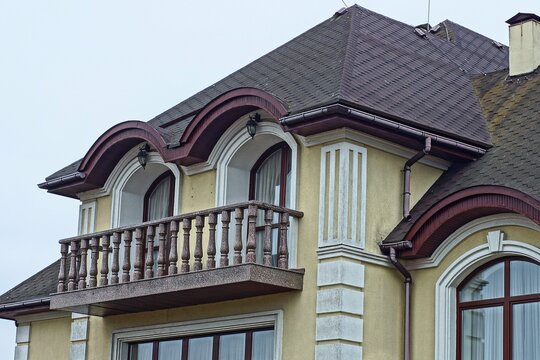 part privat of expensive large modern with yellow walls beautiful with brown roof with tiles and balcony with black retro lanterns and windows cottage daytime against gray sky