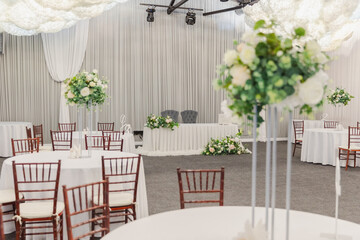 Decorated interior for festive event. Fancy table set for dinner with white flower composition in restaurant, luxury interior background. Wedding elegant banquet decoration arranged by catering