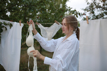 pregnant girl in the garden on a background of white fabric. woman hanging laundry on a line in the...