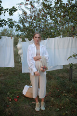Naklejka premium pregnant girl in the garden on a background of white fabric. woman hanging laundry on a line in the garden after washing. pregnant woman on a background of white sheets. woman stands outdoors
