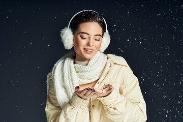 Fototapeta premium A joyful woman plays with falling snowflakes while bundled in warm winter attire.