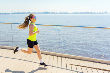 A Woman Jogs Along a Waterfront Path on a Sunny Day, Enjoying the Scenic View of the Water and...