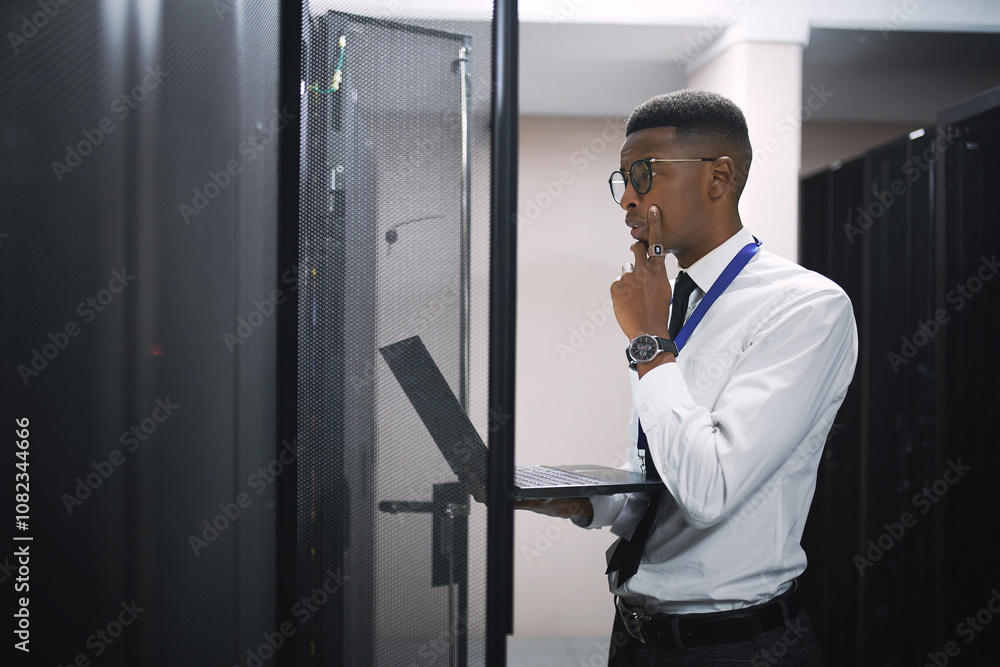 Poster Black man, engineer and troubleshooting with laptop in server room for software, hardware or network repair. Male person, IT technician or thinking with computer for problem solving or system backup
