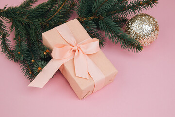 Christmas, festive background. Rose gift box with pink ribon on green coniferous branches on a pink background. Top view