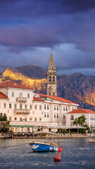 Fototapeta premium In Perast, Montenegro, just after sunset, a dramatic cloud hovers over the old town. The scene captures the tranquil waters, historic architecture, and mountains shrouded in evening light.